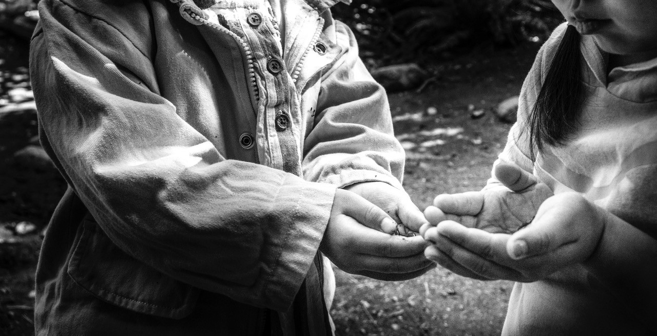 Photo Credit: Catalina Baeza Hidalgo . Photo is black and white and shows two children cupping their hands towards one another.